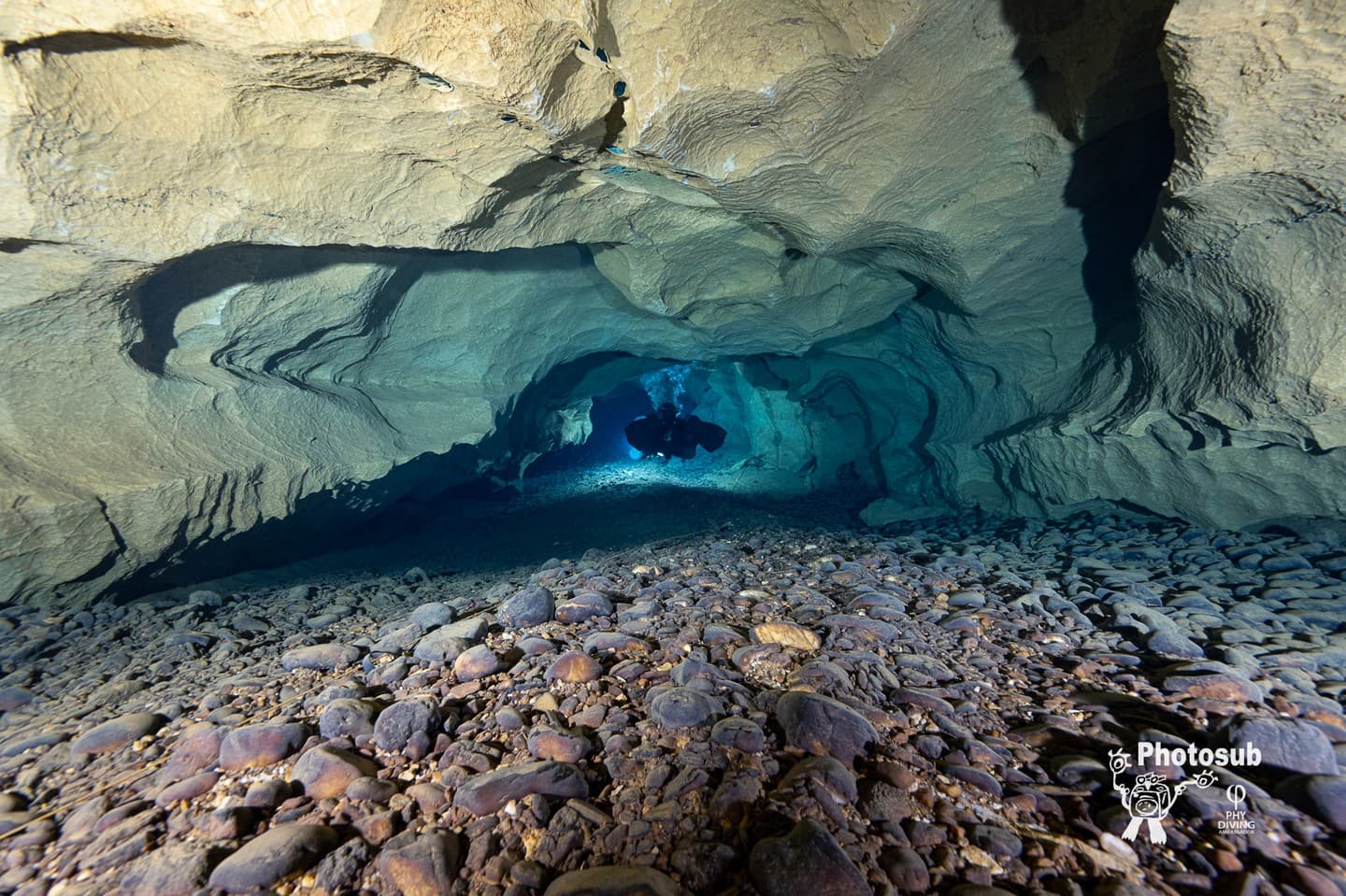 Diver silhouetted against a blue arch opening in a cave with rocky floor in foreground