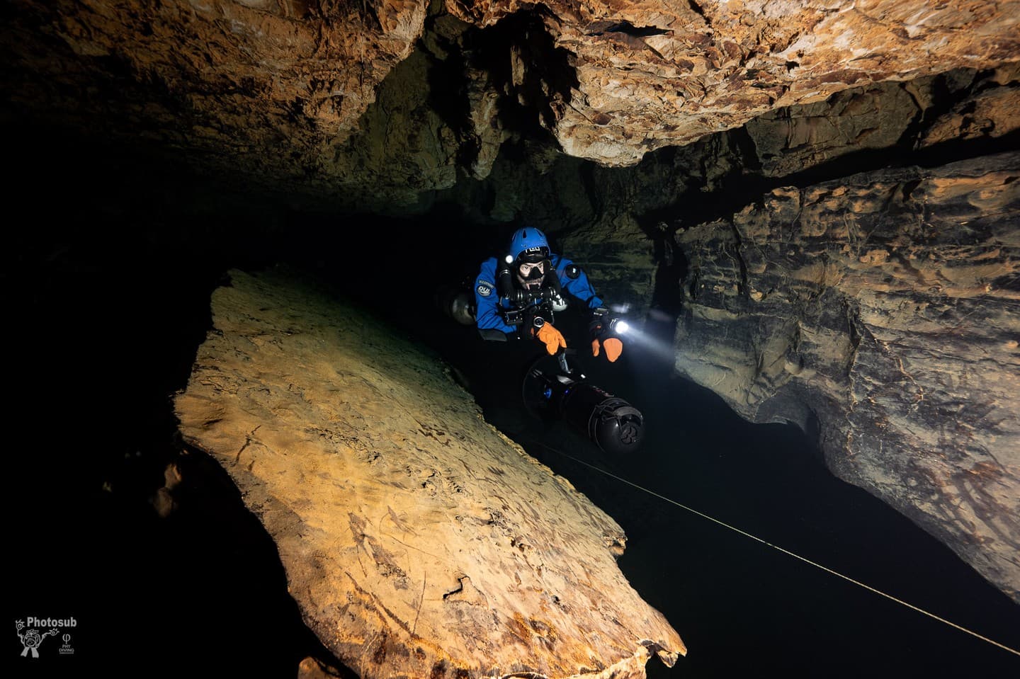 Cave diver with blue helmet and guideline navigating along a rocky overhead passage