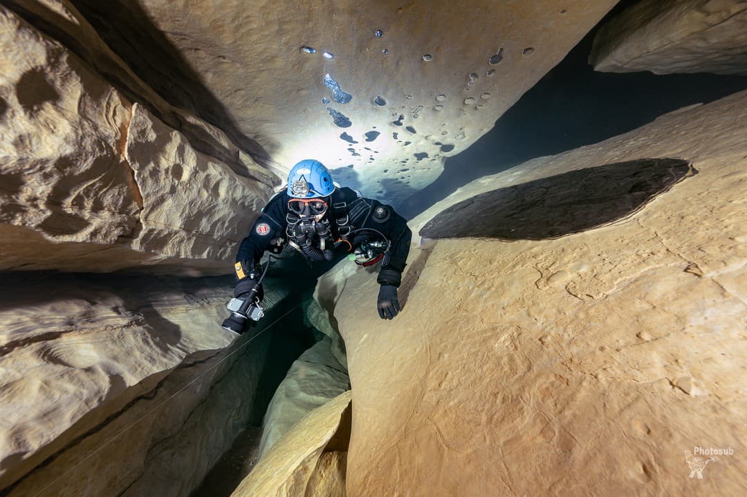 Cave diver ascending vertically through a narrow rock crack with perfect horizontal trim