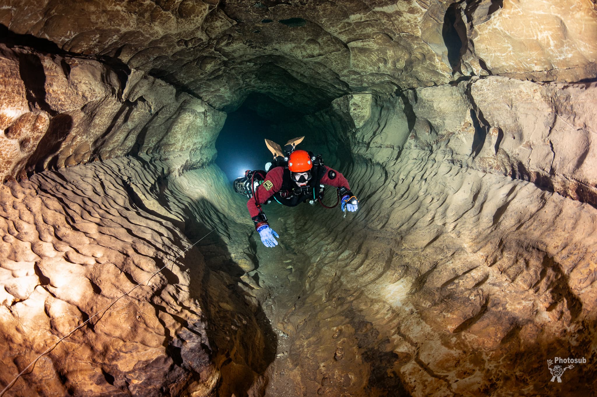 Cave diver navigating through a perfectly circular tubular cave passage with rippled sandy floor